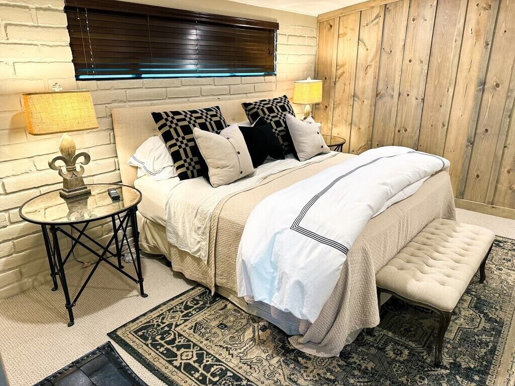 A bedroom with a bed, bedside tables, a lamp, a patterned rug, and a wooden wall panel.