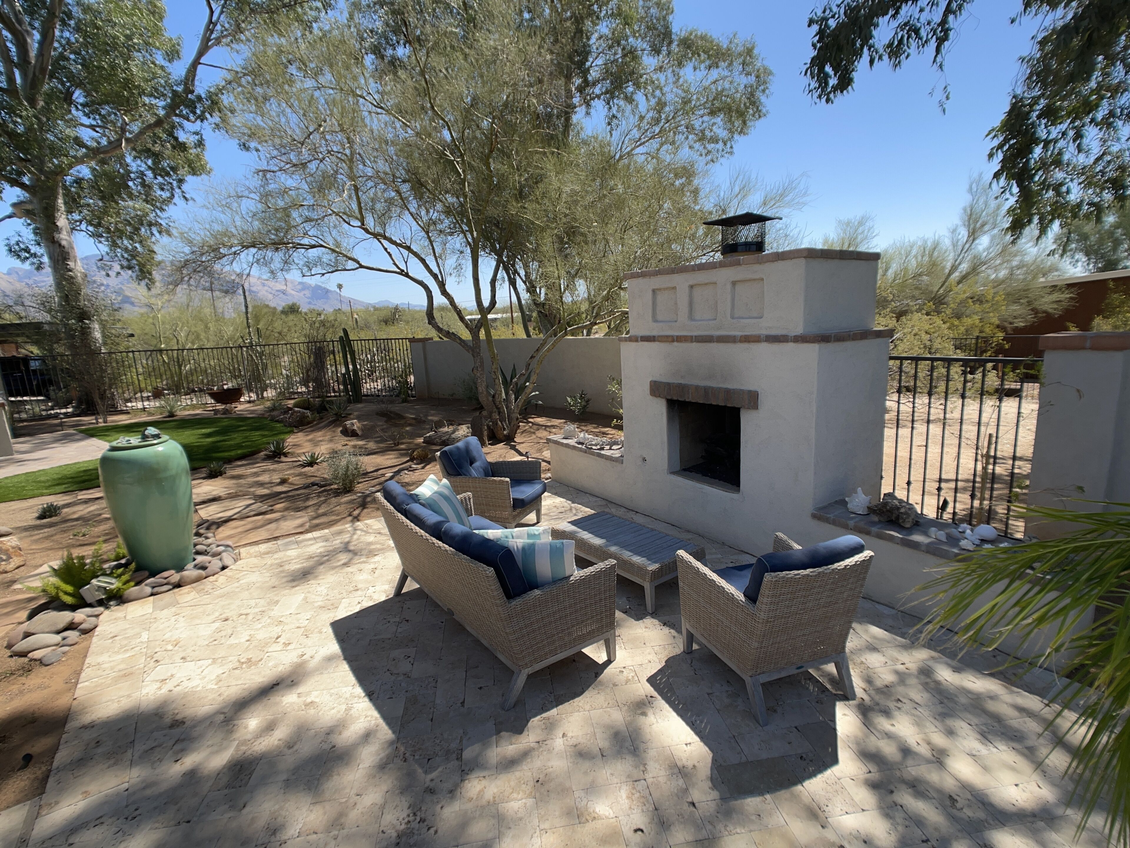 An outdoor patio with wicker furniture, a stone-tiled floor, and a stone fireplace.