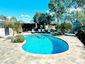 A swimming pool with a curved edge, surrounded by a paved patio area with lounge chairs and umbrellas. - Serene, tree-shaded, mid-century retreat with beautiful views of the Catalinas (Tucson)