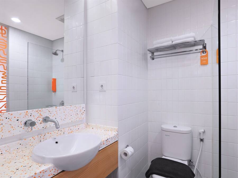 A modern bathroom with a white sink, a mirror, a toilet, and a shower area.