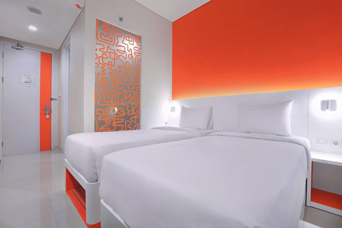 Une chambre d’hôtel avec deux lits, une décoration aux couleurs blanche et orange, et un design moderne.