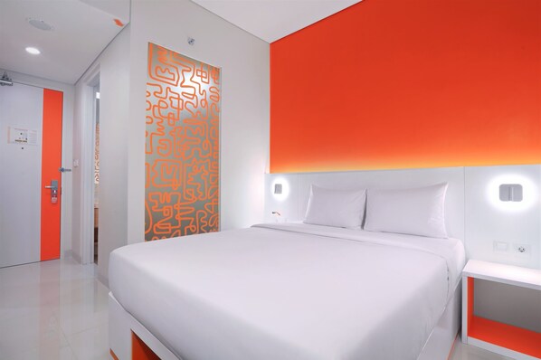 Une chambre d’hôtel moderne avec un grand lit, une table de chevet et un mur d’accent d’un orange vif.