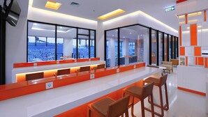 Una moderna zona de recepción con una larga barra, asientos y puertas de cristal que dan a un balcón con vistas a la ciudad.
