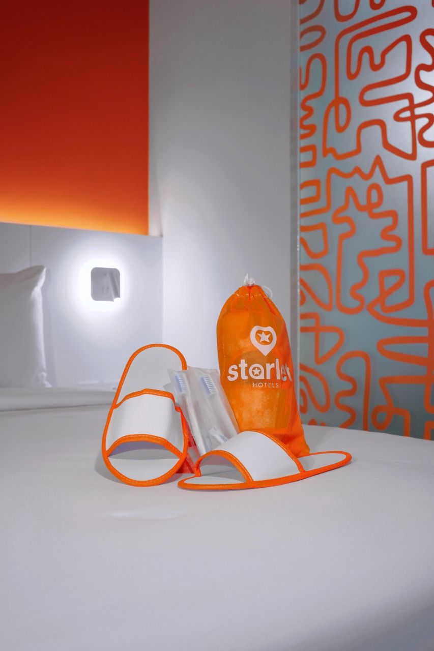 A hotel room with a bed, a nightstand, a wall-mounted light, and a patterned curtain.