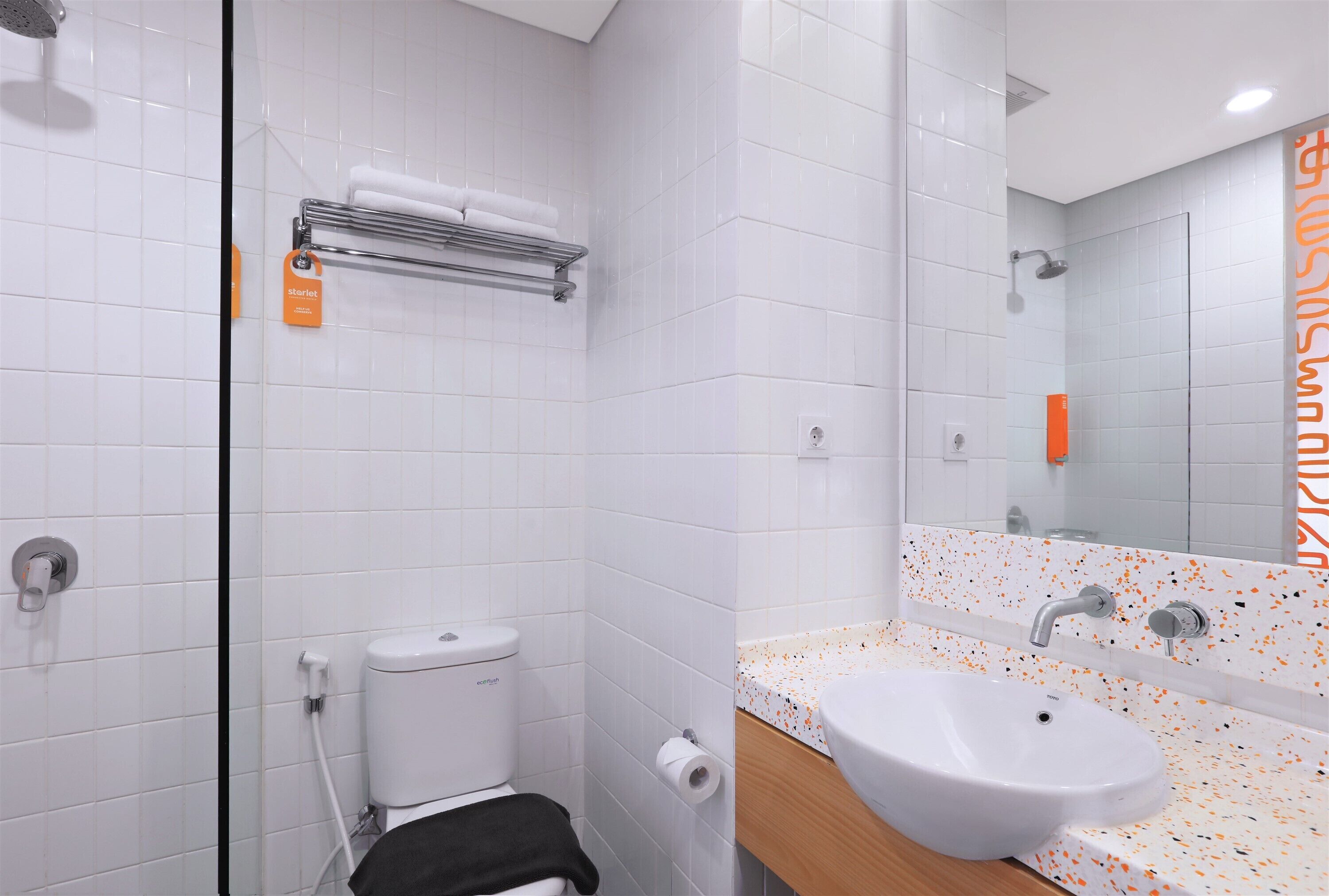Een moderne badkamer met witte tegels, een douche, toilet, wastafel en spiegel.