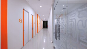 Un pasillo con puertas numeradas, una pared de vidrio con patrones abstractos y un piso limpio y reflectante.