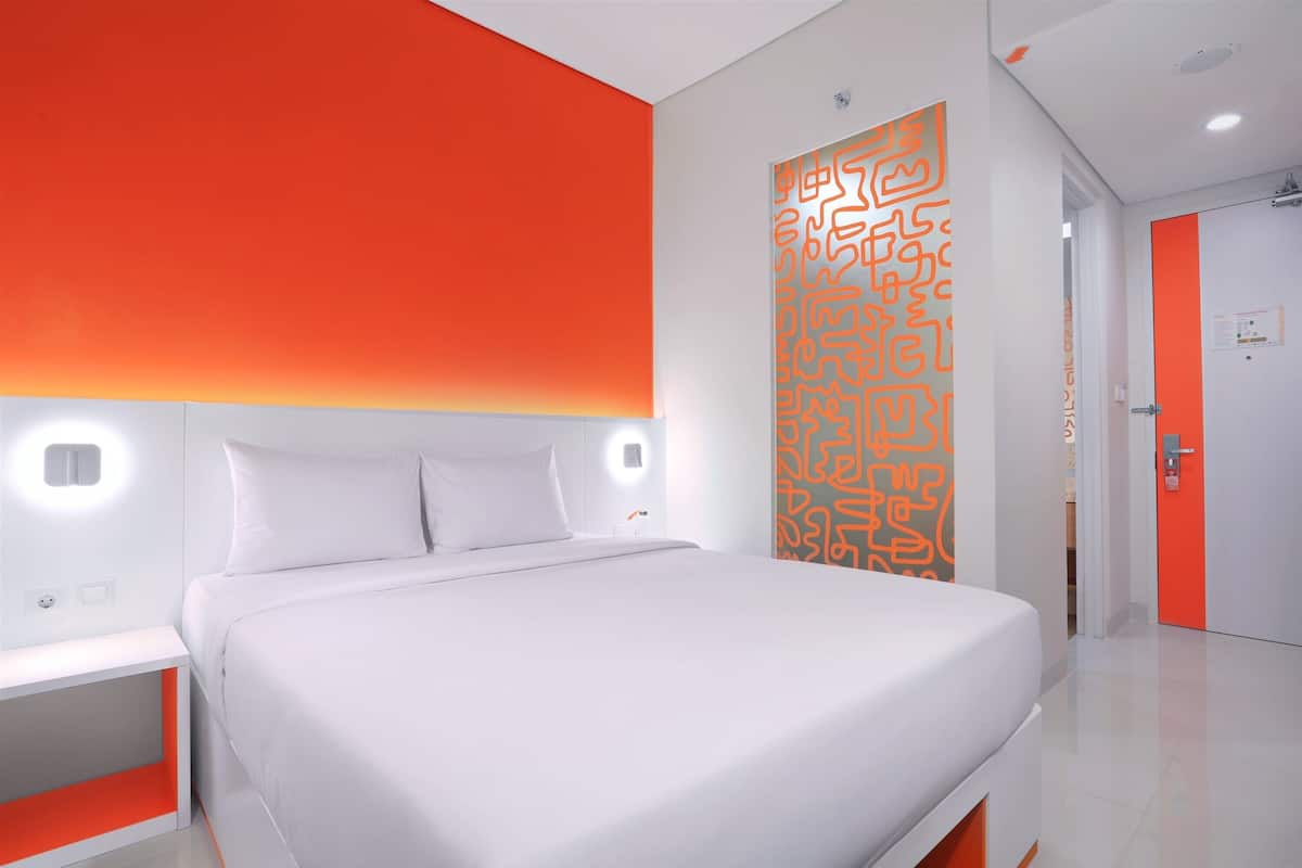 Une chambre d’hôtel moderne avec un grand lit, des murs blancs et un mur d’accent d’un orange vif.