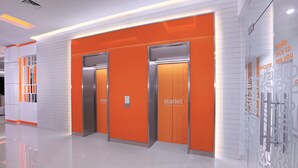 Vestíbulo moderno de hotel con tres ascensores, una paleta de colores limpia en blanco y naranja, y un mensaje de bienvenida en la pared.