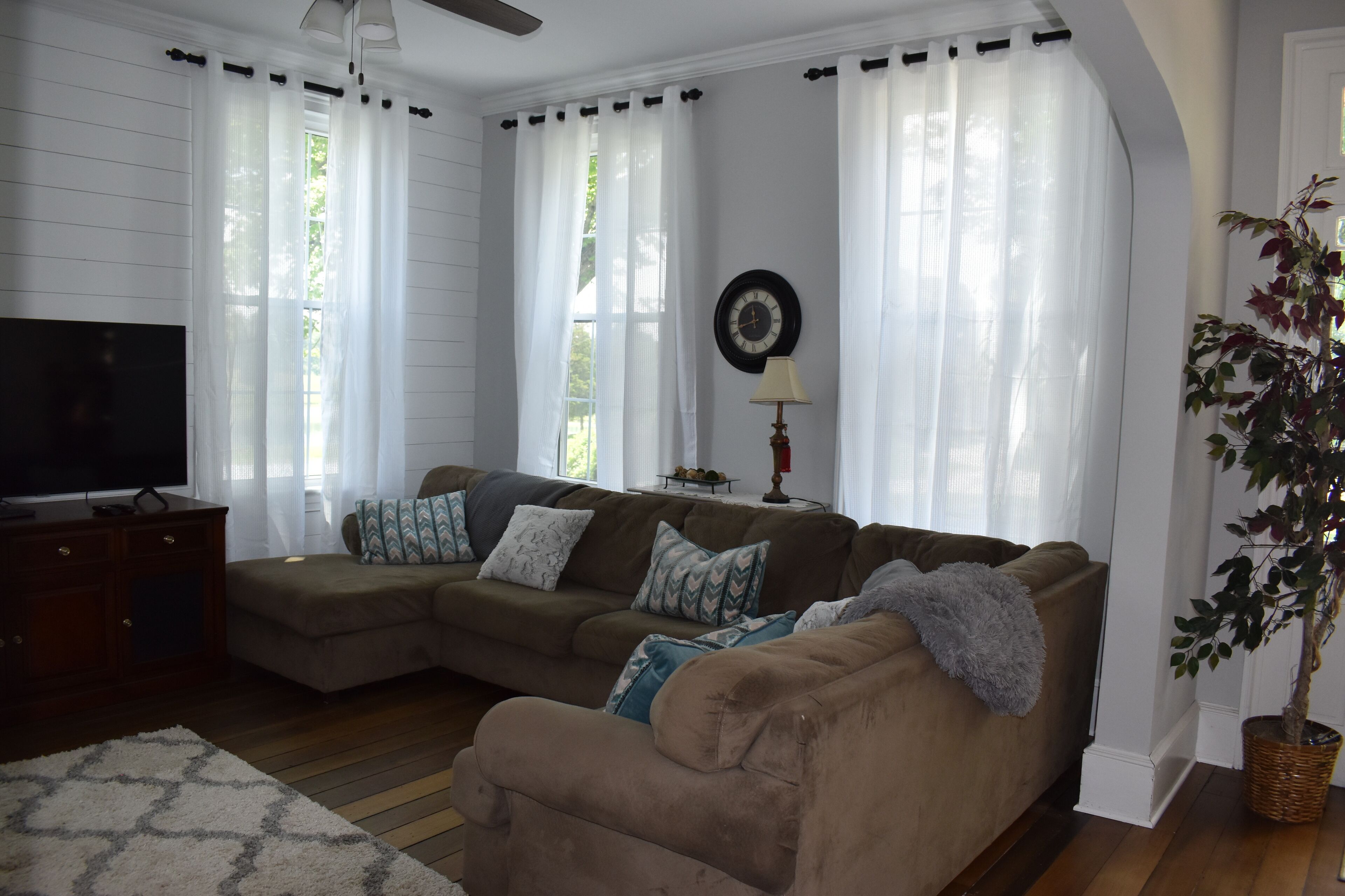 A living room with a sectional sofa, a flat-screen TV, a lamp, and a potted plant.