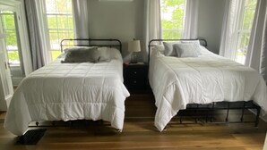 Un dormitorio con dos camas, un ventilador de techo y ventanas amplias.