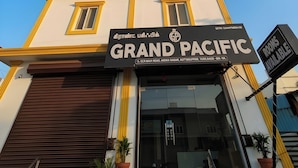 A hotel named 'Grand Pacific' with a sign in Tamil and English, a modern facade, and a sign indicating rooms are available. - Grand Pacific (Vanur)