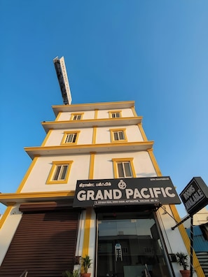 Hotel 'Grand Pacific' con un cartel en tamil e inglés, fachada moderna y un letrero que indica habitaciones disponibles.