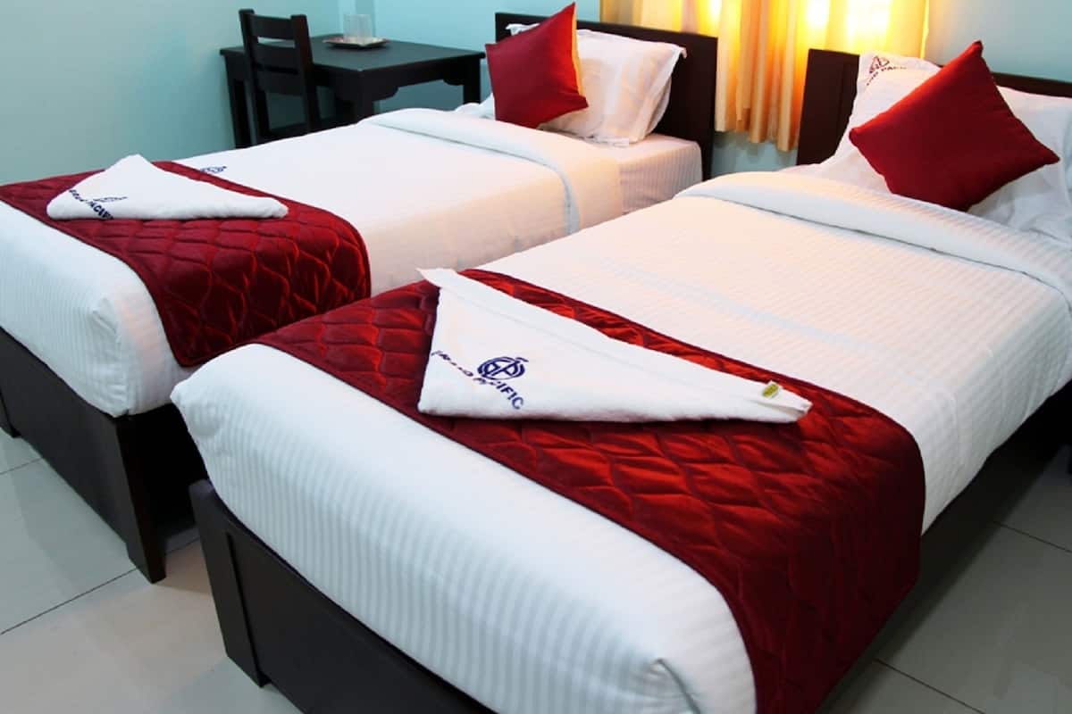 Zwei Betten mit rot-weißer Bettwäsche, ein kleiner Tisch und ein Stuhl in einem Hotelzimmer.