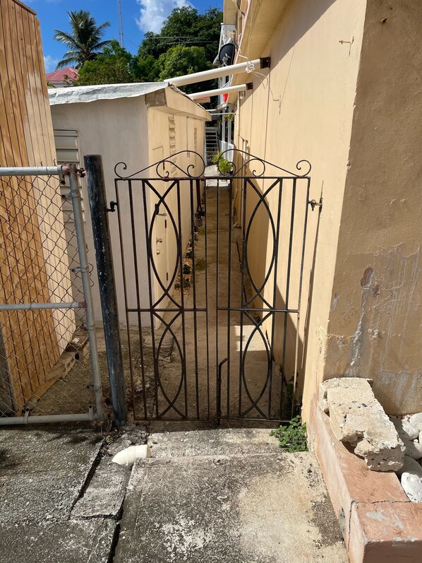 A gated entrance to a property with a narrow pathway leading to a building. - Cozy & Comfy in Paradise (St Thomas)