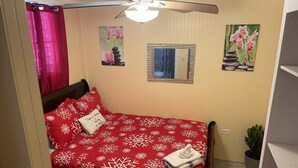 A bedroom with a bed, a ceiling fan, a window, and a wall with two paintings.