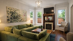 A living room with a sectional sofa, a fireplace, a television, and a large abstract painting. - New Renovated 2BR Highland Home Hot Tub Playground (Louisville)