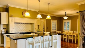 Una cocina con isla central, taburetes de bar blancos, iluminación colgante y una zona de comedor con mesa y sillas.