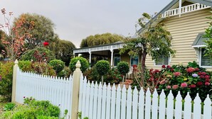 Una casa con valla de piquetes blancos, un porche y un jardín con hortensias.