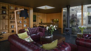A spacious living room with a leather sofa, a wooden bookshelf, and a stone fireplace. - Fusilier Cottage Battery Point (Battery Point)