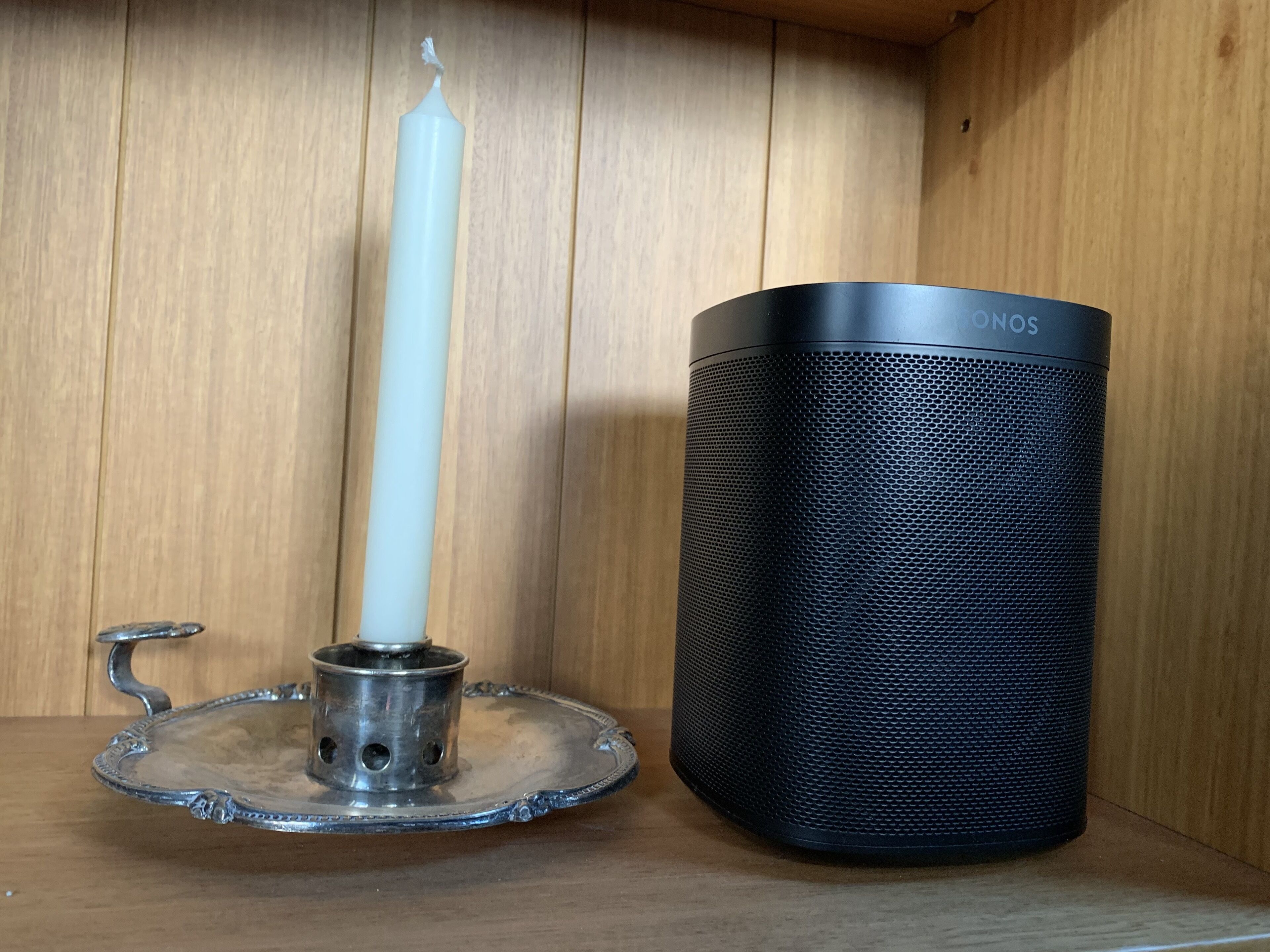 A white candle on a metal holder and a black cylindrical container with a textured surface.