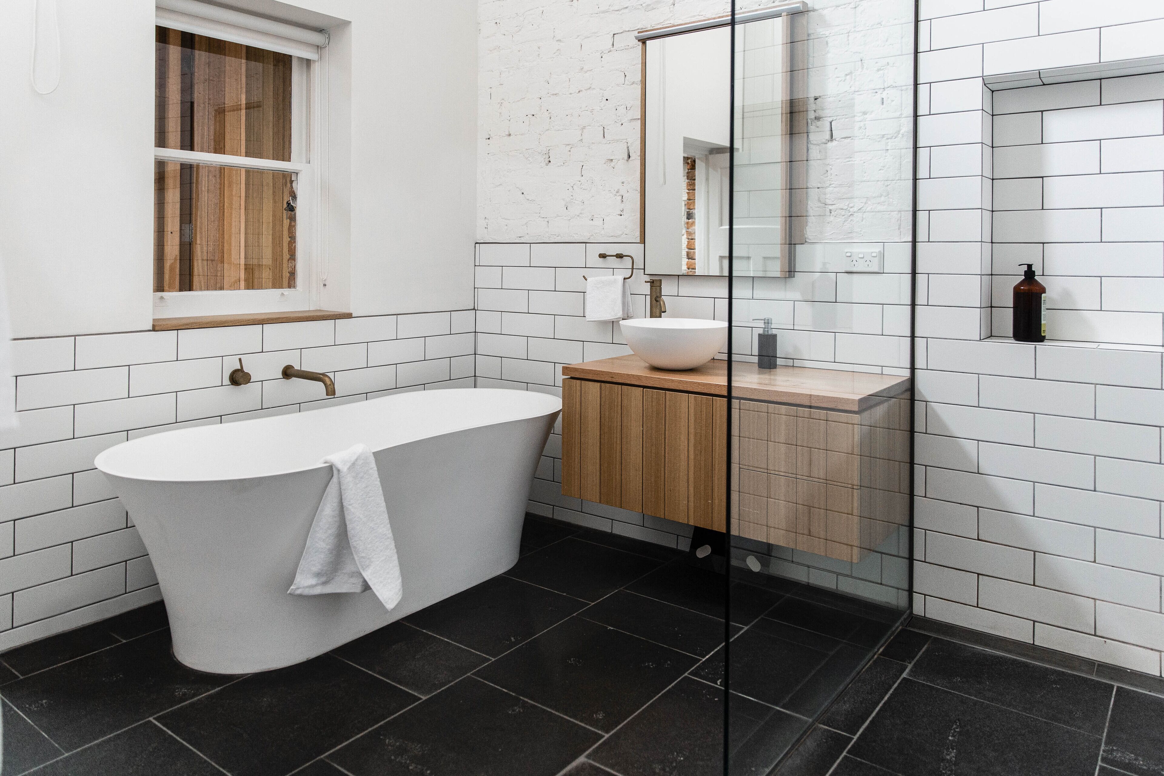 Un baño moderno con una bañera independiente, un tocador de madera, un lavabo blanco y un espejo grande.