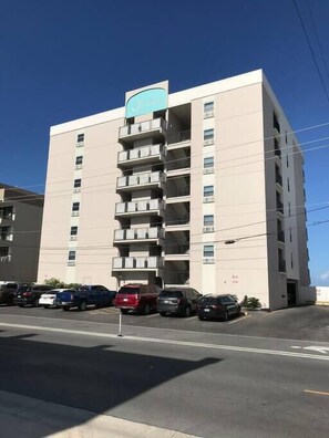 A multi-story building with a flat facade, several balconies, and a parking lot in front.