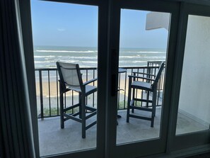 A balcony with two chairs and a table, overlooking a beach with waves. - Beachfront 4th floor, king, private balcony, pool, hot tub, BBQ (South Padre Island)