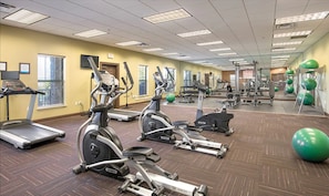 Une salle de sport équipée de tapis de course, de vélos elliptiques et de ballons d’exercice.
