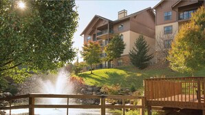 A multi-story building with balconies, a wooden deck, and a pond with a fountain. - Great Smokey Mountains Resort - Pigeon Forts Condo  (Pigeon Forge)
