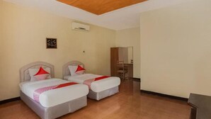 Ein Hotelzimmer mit zwei Betten, einer Holzbalkendecke, einer Klimaanlage und einem kleinen Tisch mit Stühlen.