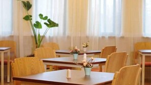 A dining area with wooden tables and chairs, a large green plant, and a window with sheer curtains. - Home Inn Hotel Beijing Tongzhou Xinhua South Road (Tongzhou)