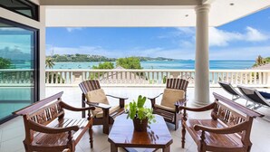 A balcony with wooden furniture and a view of the ocean. - Luxury Beachfront Tai Pan Villa (Wichit)