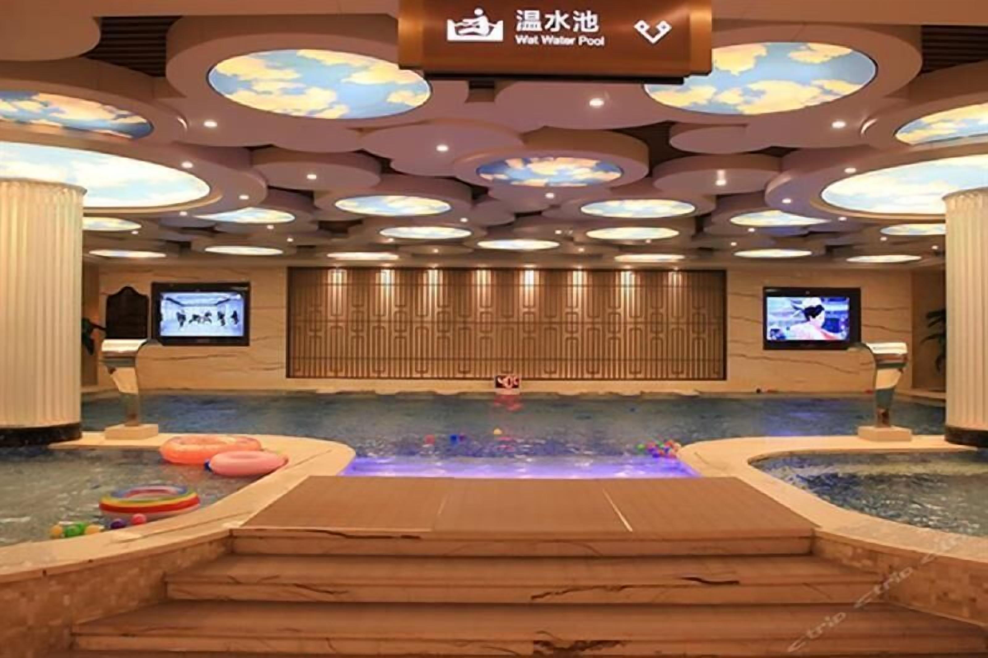 Un vestíbulo de hotel con una amplia piscina interior, un cartel para la piscina de agua tibia y una pantalla de televisión.