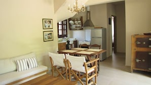 Un comedor con una mesa y sillas de madera, un sofá con cojines a rayas, y una cocina al fondo.