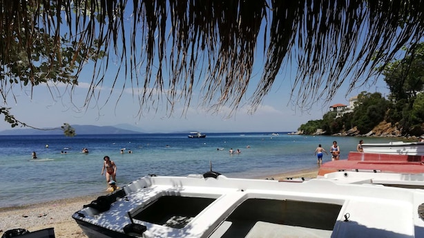 Una playa con barcos, gente nadando y una vista despejada del mar.