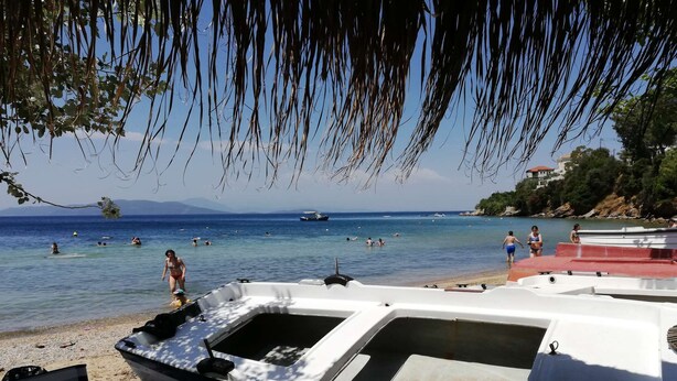 Una playa con barcos, gente nadando y una vista despejada del mar.