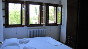 Ein Schlafzimmer mit einem Bett, einem Heizkörper und drei offenen Fenstern mit Holzrahmen.
