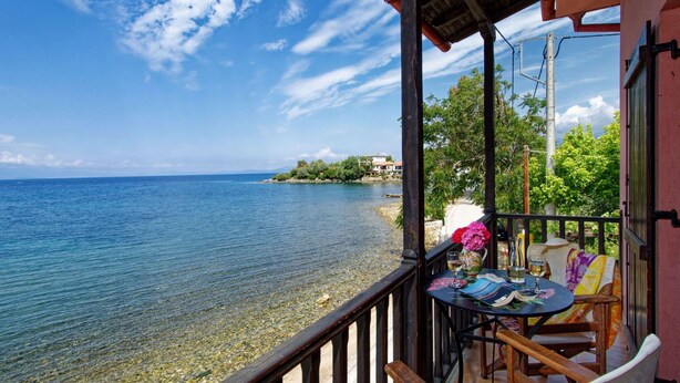 Ein Balkon am Meer mit einem Tisch für zwei Personen, mit Blick auf ruhiges Meer und eine entfernte Küste.