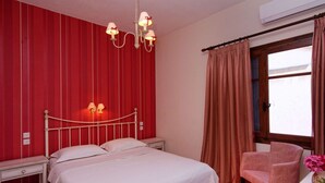 Ein Schlafzimmer mit Bett, Sessel, Nachttisch, einer Kristallleuchtre und einem Fenster mit Vorhängen.