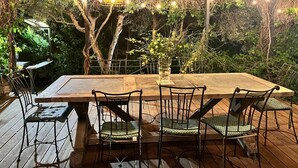 An outdoor dining area with a wooden table and chairs, surrounded by greenery and string lights. - Belle Villa au Coeur des Alpilles (Maussane-les-Alpilles)