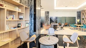 A modern library with bookshelves, a round wooden table, and comfortable seating. - Green Oriental Hotel (Shenzhen Pinghu South China City Hehua subway station) (Shenzhen)