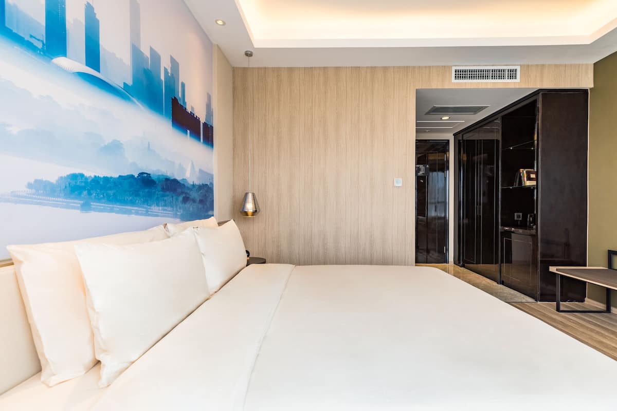 Ein modernes Hotelzimmer mit großem Bett, einer Stadtlandschaftsmalerei, einer Wand mit Holzapplikationen und einem separaten Badezimmerbereich.