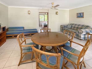 A room with a round wooden table surrounded by wicker chairs, a sofa, and a bench. - Alma Bay Holiday Unit 2-BOM (Arcadia)