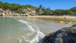 Ein Strand mit klarem Wasser, Felsen und einigen Kajaks.