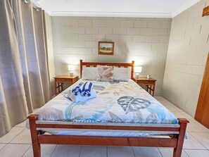 Uma cama com colcha floral, duas mesas de cabeceira com abajures, um painel de cabeceira de madeira e uma parede com padrão de tijolos.