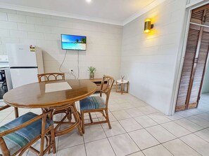 A dining area with a round table, chairs, a television mounted on the wall, and a small potted plant.