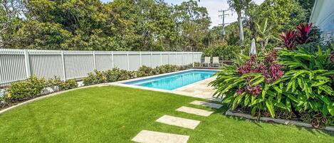 A backyard with a swimming pool, a white fence, and a well-maintained lawn.