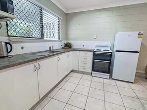Uma cozinha com armários brancos, chaleira de aço inoxidável, fogão e geladeira.