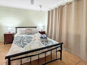 A bedroom with a bed, nightstands, a ceiling fan, and a curtain.