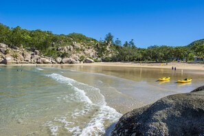 A beach with clear water, rocks, and a few kayaks.